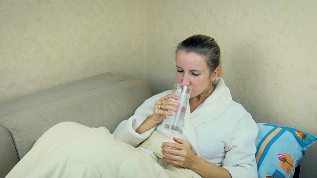 一个生病的年轻女孩在家里的沙发上喝一片起泡的阿司匹林。视频素材