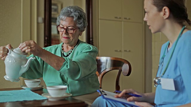 年长的妇女和家庭看护聊天，在家喝茶。视频素材