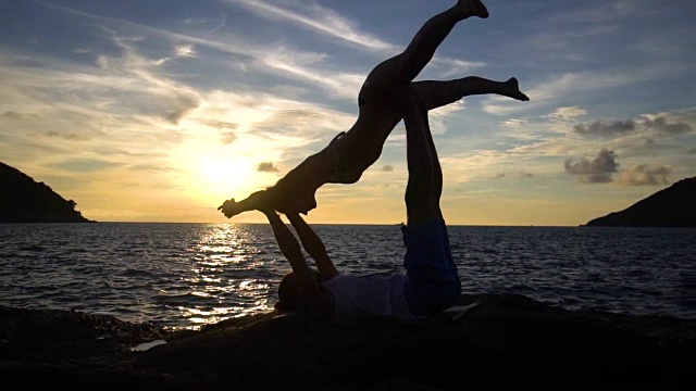 一对夫妇在日落时在海边的岩石上做瑜伽。视频素材