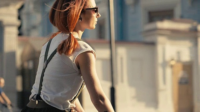 红发女子骑自行车在城市道路上的背景建筑慢动作视频素材