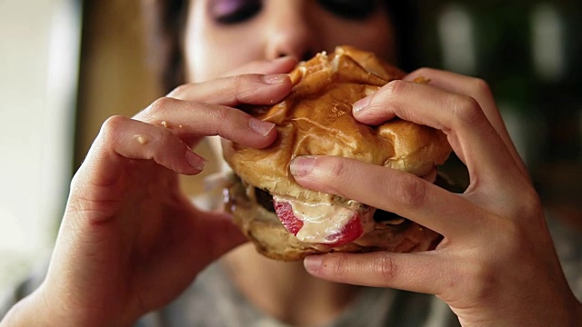年轻女子咬大美味多汁的汉堡在咖啡馆的特写镜头。Slowmotion拍摄视频素材