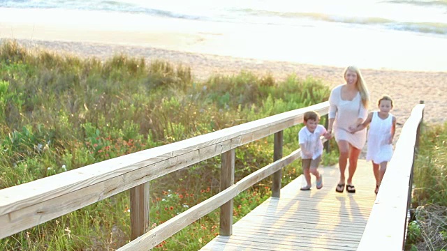 母亲和两个孩子在海滩的木栈道上视频素材
