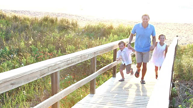 父亲和两个孩子在海滩的木栈道上视频素材