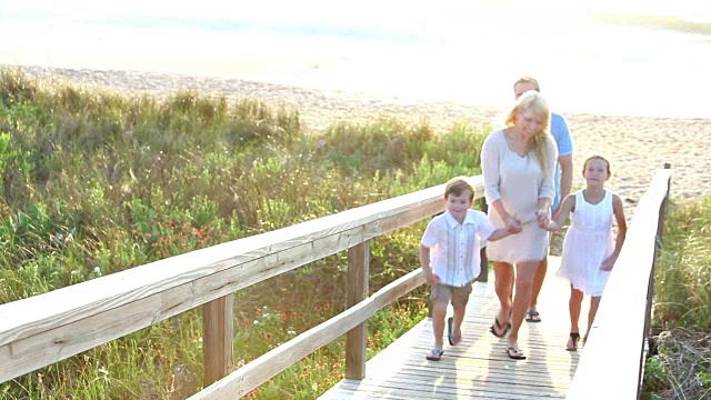 一家人带着两个孩子在海滩的木制人行道上视频素材