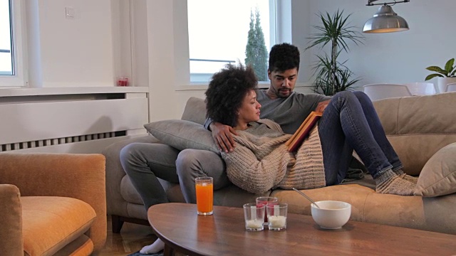 年轻的非裔美国夫妇在沙发上放松，一边看书，一边交流。视频素材