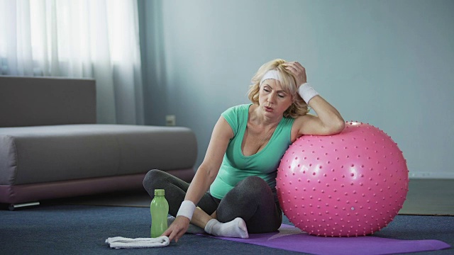 疲惫的中年女性在瑜伽垫上休息后，积极的家庭锻炼，呼吸困难视频购买