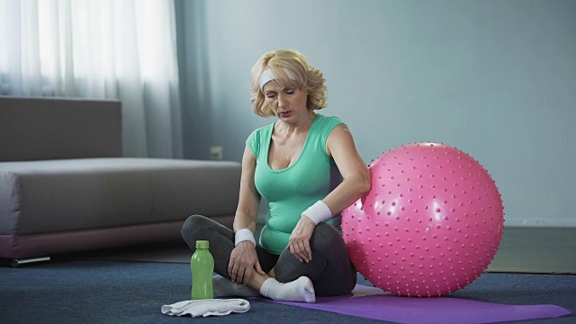运动高级妇女坐在瑜伽垫上，按摩她的背部，腰痛视频素材
