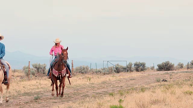 牛仔和女牛仔在一条土路上骑马视频素材