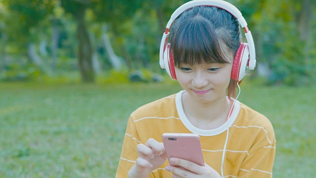 女人开心地笑着，在公园里用手机听音乐视频下载