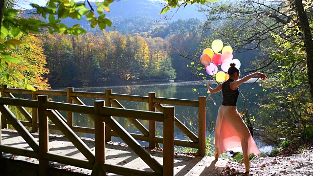 秋天，美丽的芭蕾舞演员在湖边的木制码头上舞动着彩色气球视频下载