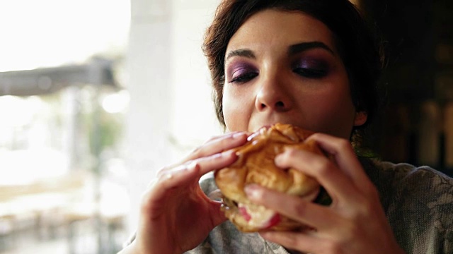 近距离观看年轻女子咬大可口的汉堡在咖啡馆。Slowmotion拍摄视频素材