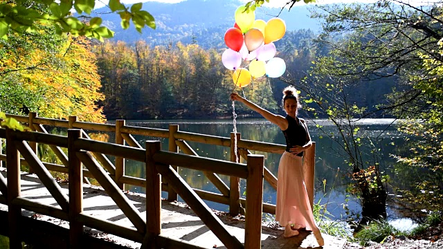 秋天，美丽的芭蕾舞演员在湖边的木码头上与彩色气球一起跳舞(电影图片)视频下载