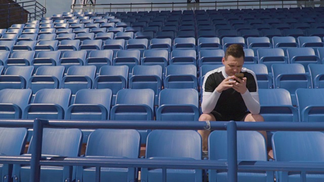 橄榄球运动员站在一个空看台上，看着电话视频下载