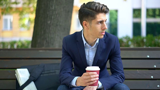年轻人在公园长椅上喝着咖啡放松视频下载