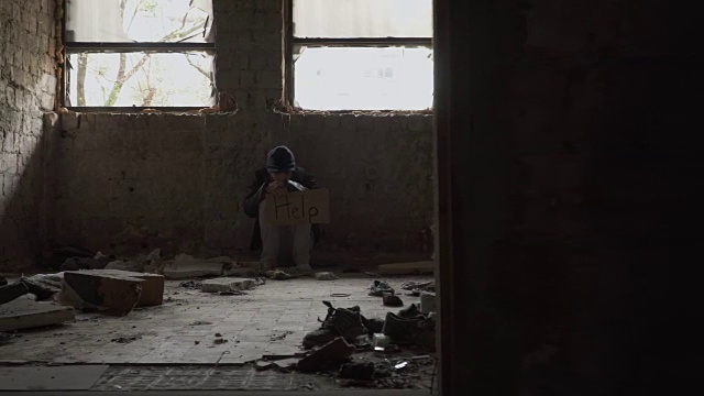 饥寒的无家可归者拿着盘子坐在废弃的建筑里视频下载