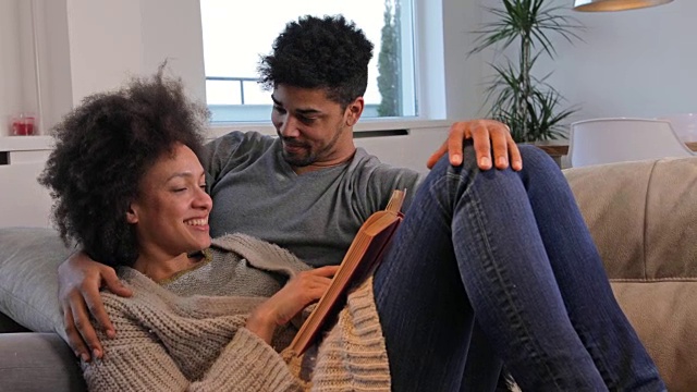 一对年轻的非裔美国夫妇在沙发上看书，互相表达爱意。视频素材
