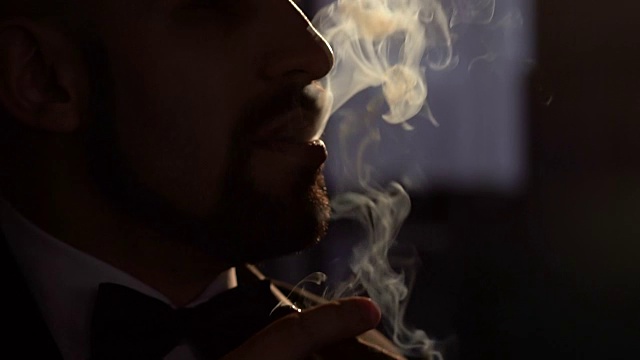 男人在黑暗中用人工照明抽雪茄。视频素材