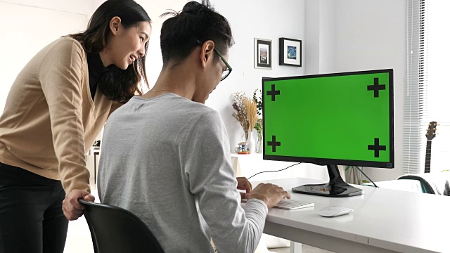两个亚洲人看着绿色屏幕的电脑视频素材