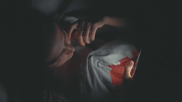 年轻女子晚上在床上玩手机视频下载