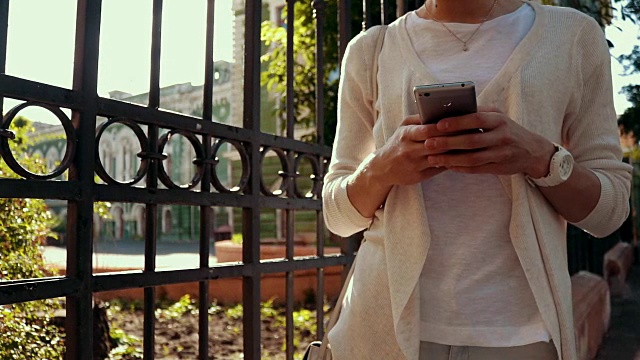 年轻苗条的女人穿着白色开襟羊毛衫在一个夏日阳光明媚的日子里使用手机，特写，慢动作视频素材