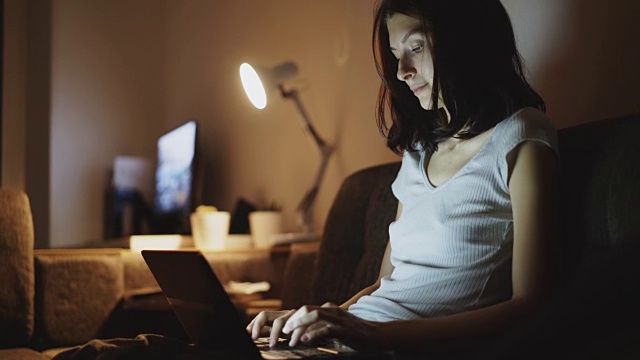 年轻专注的女人晚上在家里用笔记本电脑打字视频素材