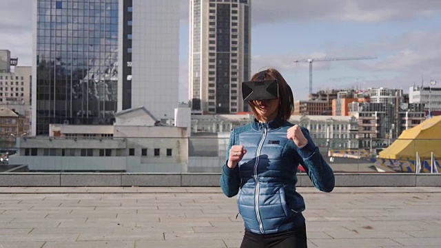 年轻的运动女性玩家戴着增强现实眼镜打拳击玩动作模拟游戏手机app，女性玩家在VR头盔中用拳头格斗，户外虚拟训练新技术视频下载