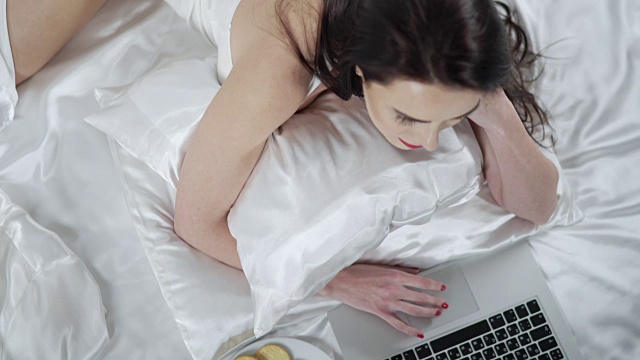 卧室里的美女躺在床上用笔记本电脑工作视频素材