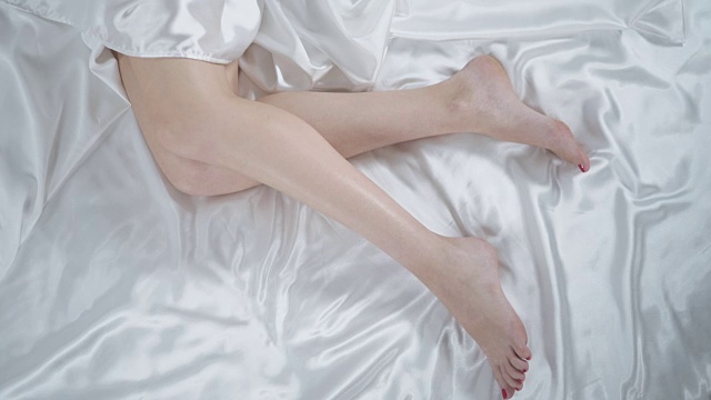 漂亮女人躺在卧室的床上。女人的腿上的白床单特写视频素材