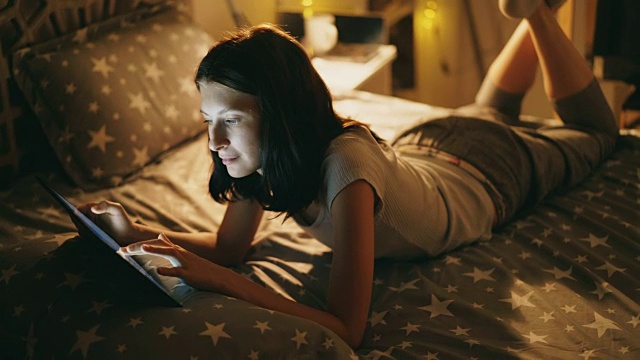 迷人的微笑女人放松在床上使用平板电脑晚上在家里视频素材