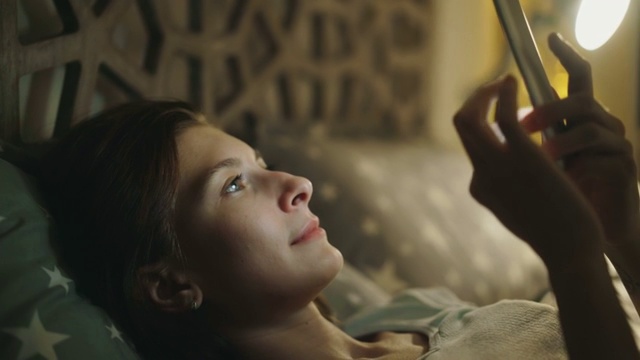 年轻微笑的女人晚上躺在家里的床上使用智能手机的特写视频素材