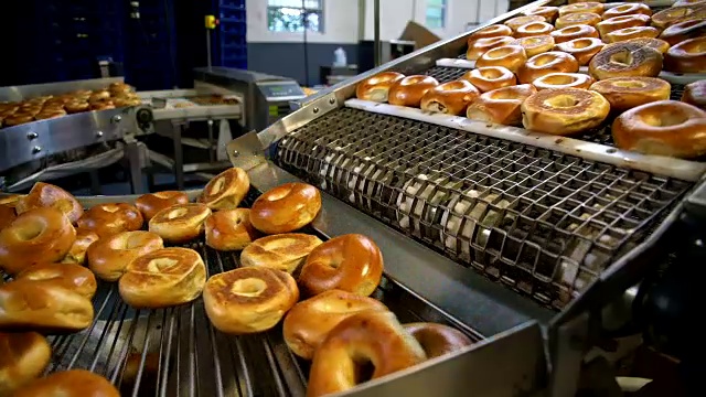 在面包房的工厂里制作新鲜又热又好吃的百吉饼-百吉饼在传送带上运输并分类。视频下载