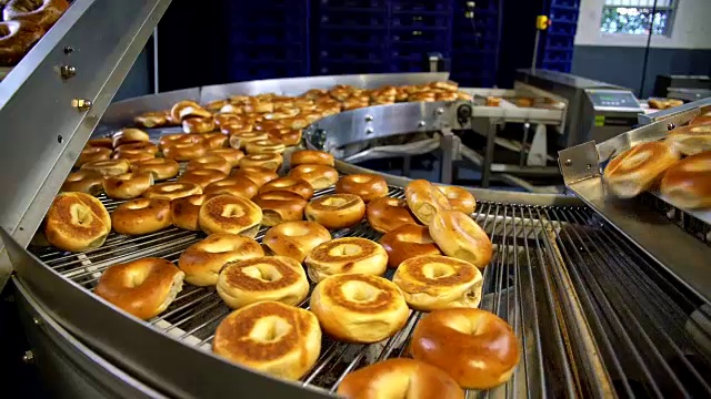 在面包房的工厂里制作新鲜又热又好吃的百吉饼-百吉饼在传送带上运输并分类。视频素材