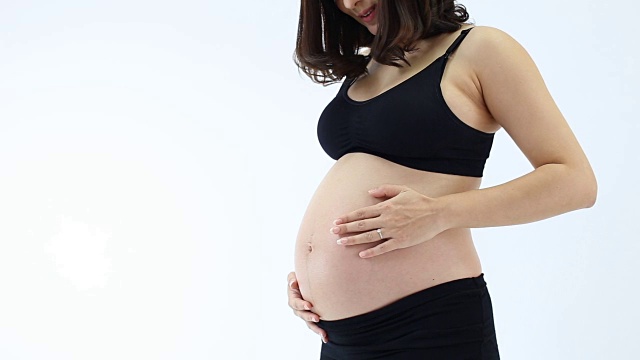孕妇抱着肚子，玩着她的孩子，在白色的背景下微笑视频素材