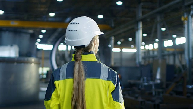以下是戴安全帽的女工走过重工业制造厂的照片。在各种金属制品项目的背景零件躺着视频素材