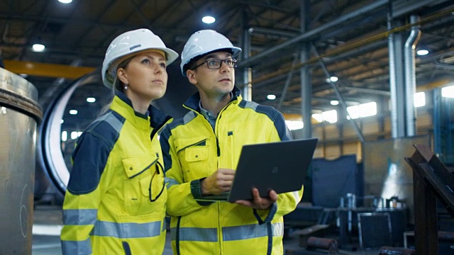 男和女工业工程师在安全帽讨论新项目，同时使用笔记本电脑。他们会做一些有表现力的手势。他们在重工业制造厂工作。长针。视频素材