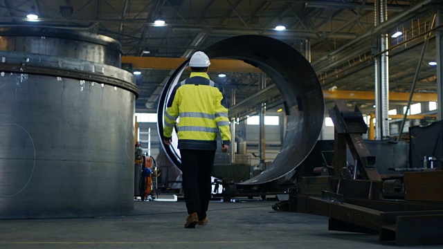 工业工程师戴安全帽、穿安全夹克穿过重工业制造工厂的各种金属加工工艺。视频素材
