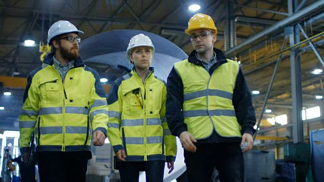 以下是三名工程师走过重工业制造厂的照片。焊接工作在进行中，各种金属制品，管道/桶组件。缓慢的运动。视频素材