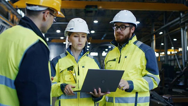 男性和女性工业工程师在使用笔记本电脑时与工厂工人交谈。他们在重工业制造工厂工作。视频素材