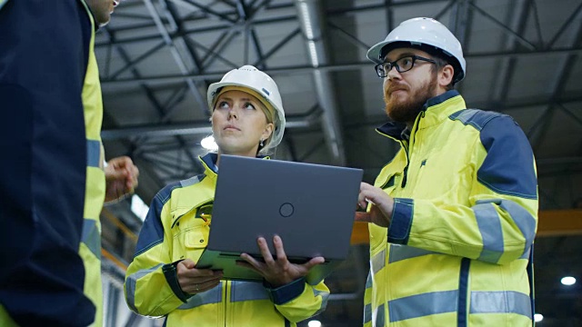 男性和女性工业工程师在使用笔记本电脑时与工厂工人交谈。他们在重工业制造工厂工作。低角度拍摄。视频素材