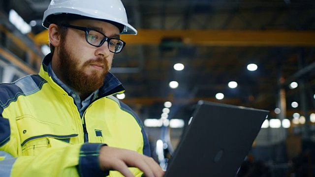 工业工程师戴安全帽穿安全服使用触屏笔记本电脑。他在重工业制造厂工作。视频素材