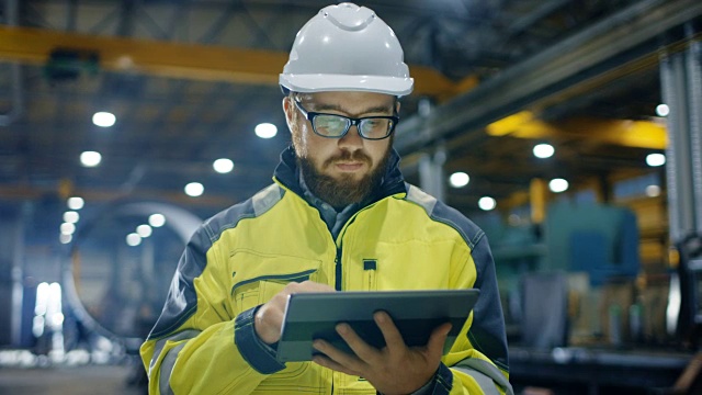 工业工程师戴安全帽穿安全服使用触屏平板电脑。他在重工业制造厂工作。视频素材