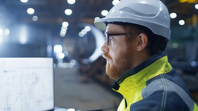工业工程师戴安全帽，安全夹克和眼镜在镜头前微笑。他在大型重工业工厂工作。视频下载