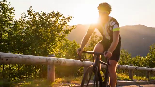 精疲力竭的公路自行车骑上坡与太阳慢慢落下的背景视频素材