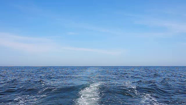 在平静的海面和晴朗的天空下，慢动作的游船轨迹视频下载