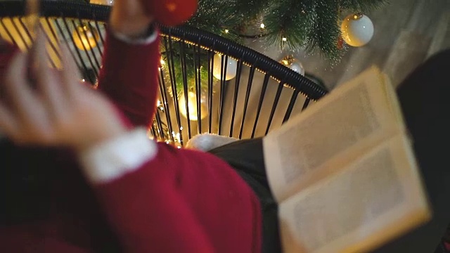 女人坐在圣诞树前的椅子上看书视频素材