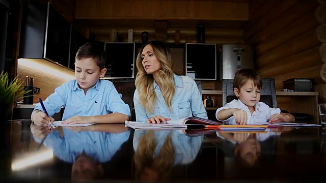 快乐的家庭，两个孩子的母亲帮助儿子做他们的家庭作业坐在厨房的大桌子视频素材