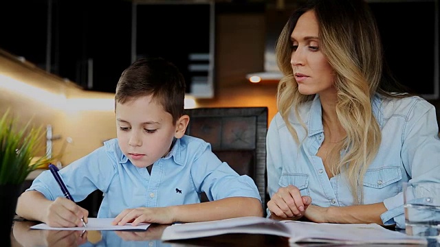 母亲微笑着帮儿子做作业，口述着课文坐在餐桌旁帮你写字视频素材