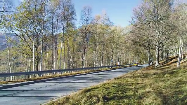 向后鸟瞰黄色老爷车行驶在五颜六色的秋天森林的道路上。秋天有橙、绿、黄、红的树林。山区街道道路的建立。4k无人机飞行建立商店视频素材