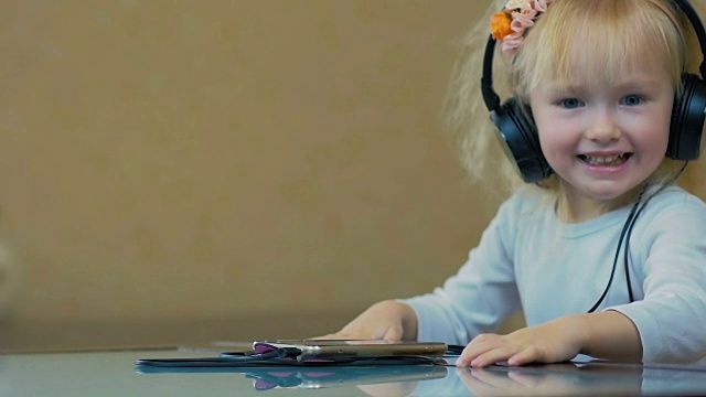慢镜头:一个三岁的小女孩戴着大耳机在家里用智能手机听音乐。视频下载