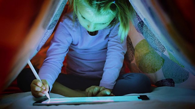金发碧眼的白人小女孩晚上在床底下用平板电脑应用进行数码着色。儿童在家里使用的现代科技。4 k的视频视频下载